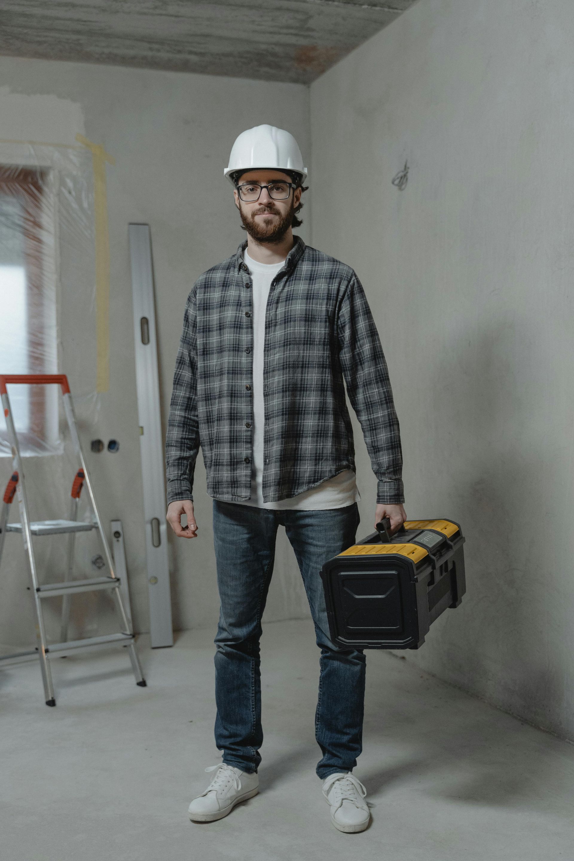 A man in a hard hat is holding a toolbox in a room.