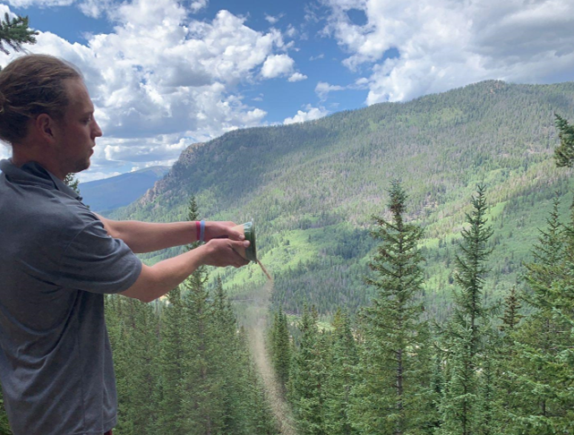 A man is standing on top of a mountain taking a picture.