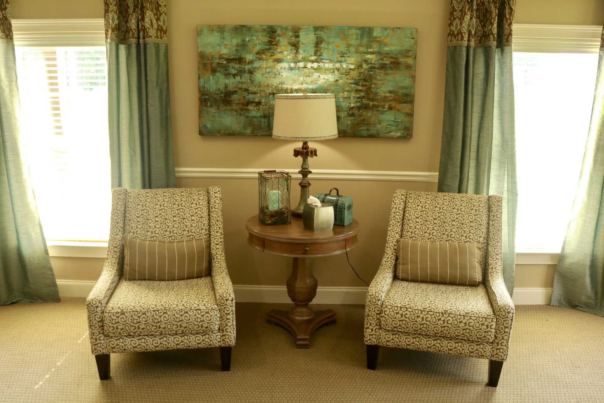 A living room with two chairs and a table with a lamp on it