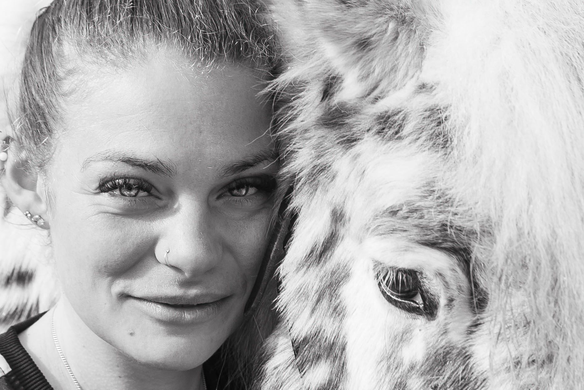 Een zwart-wit close-upportret van een persoon die zijn wang tegen de kop van een gevlekt paard drukt.