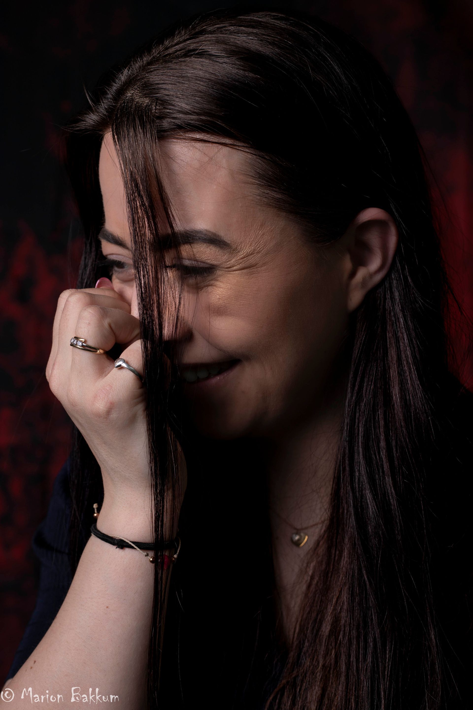 Lachende vrouw, hand bij het gezicht, haarlokken omlijsten het gezicht, gouden glans, donkere achtergrond.