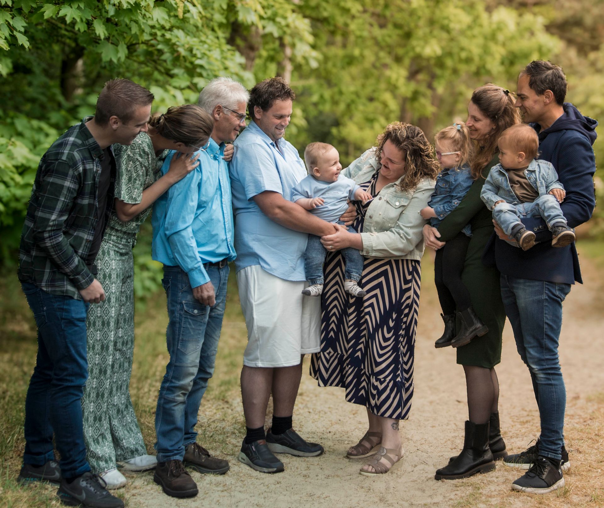 Een groep mensen in de buitenlucht, met baby's op de achtergrond. Bos op de achtergrond.