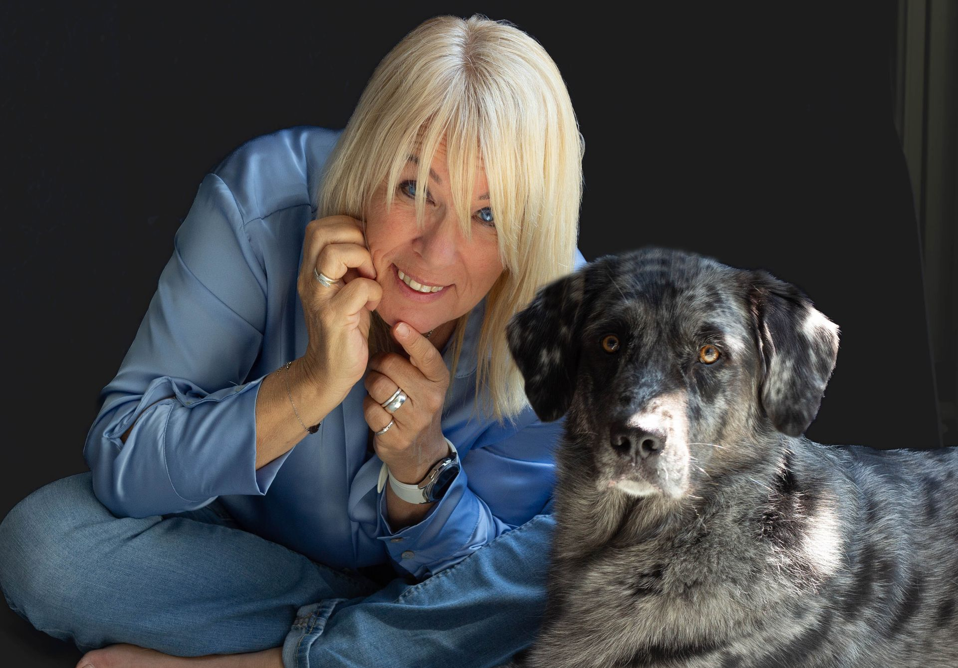 Vrouw met blond haar en een blauw shirt zit naast een hond met gevlekte grijze vacht.
