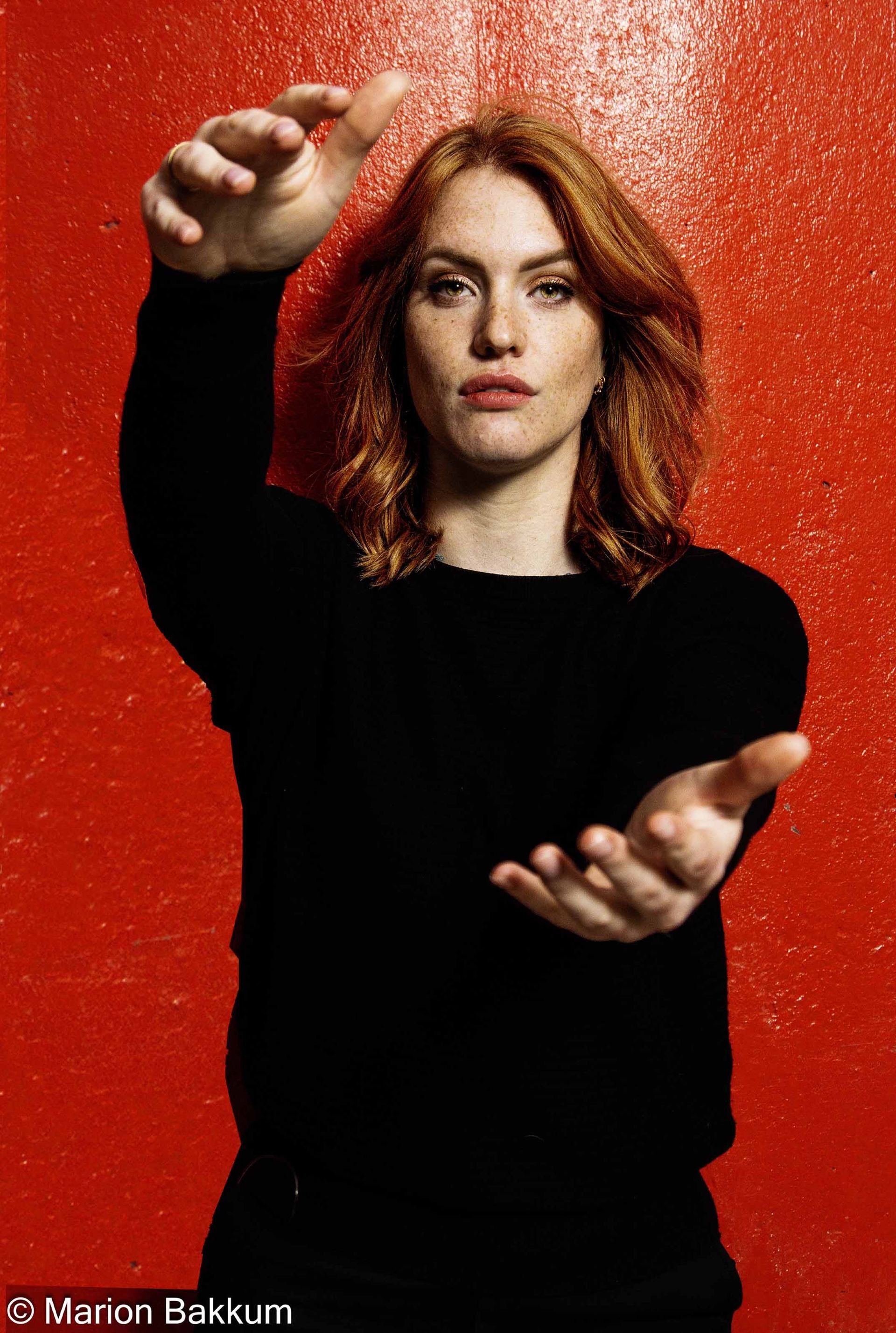 Een vrouw in een zwarte trui strekt haar handen uit voor een rode muur.