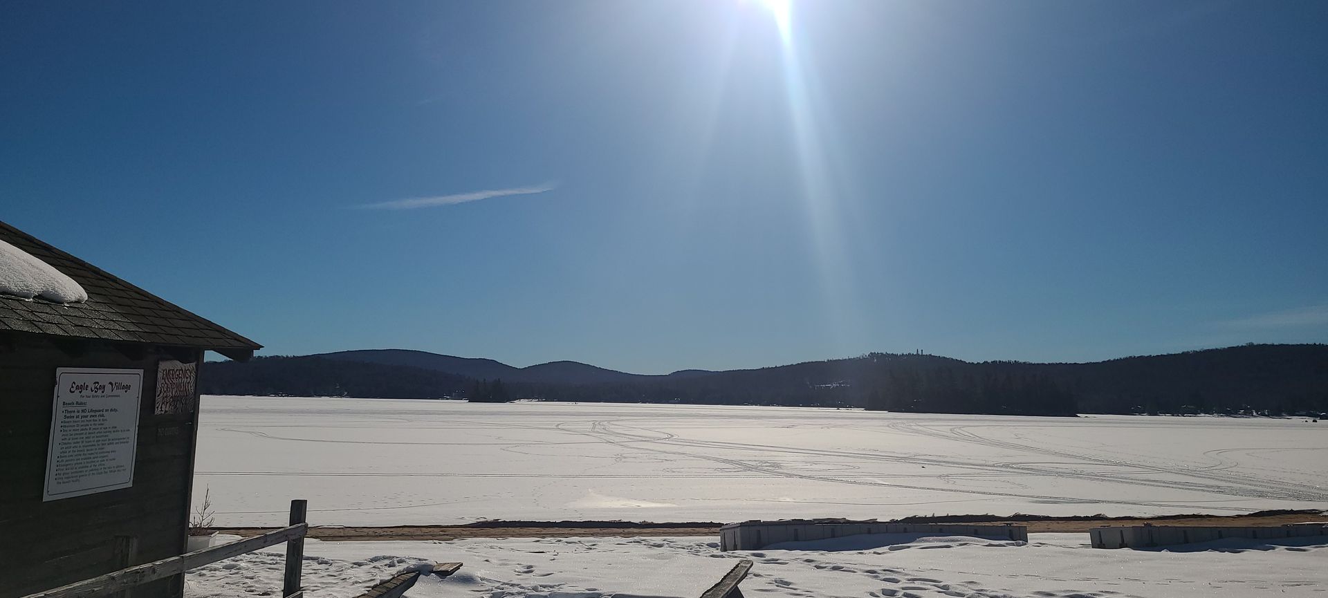 A snowy field with a small building in the foreground and a large body of water in the background.