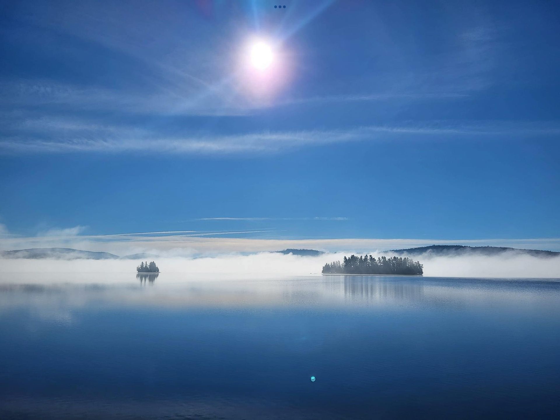A small island in the middle of a lake with the sun shining through the clouds