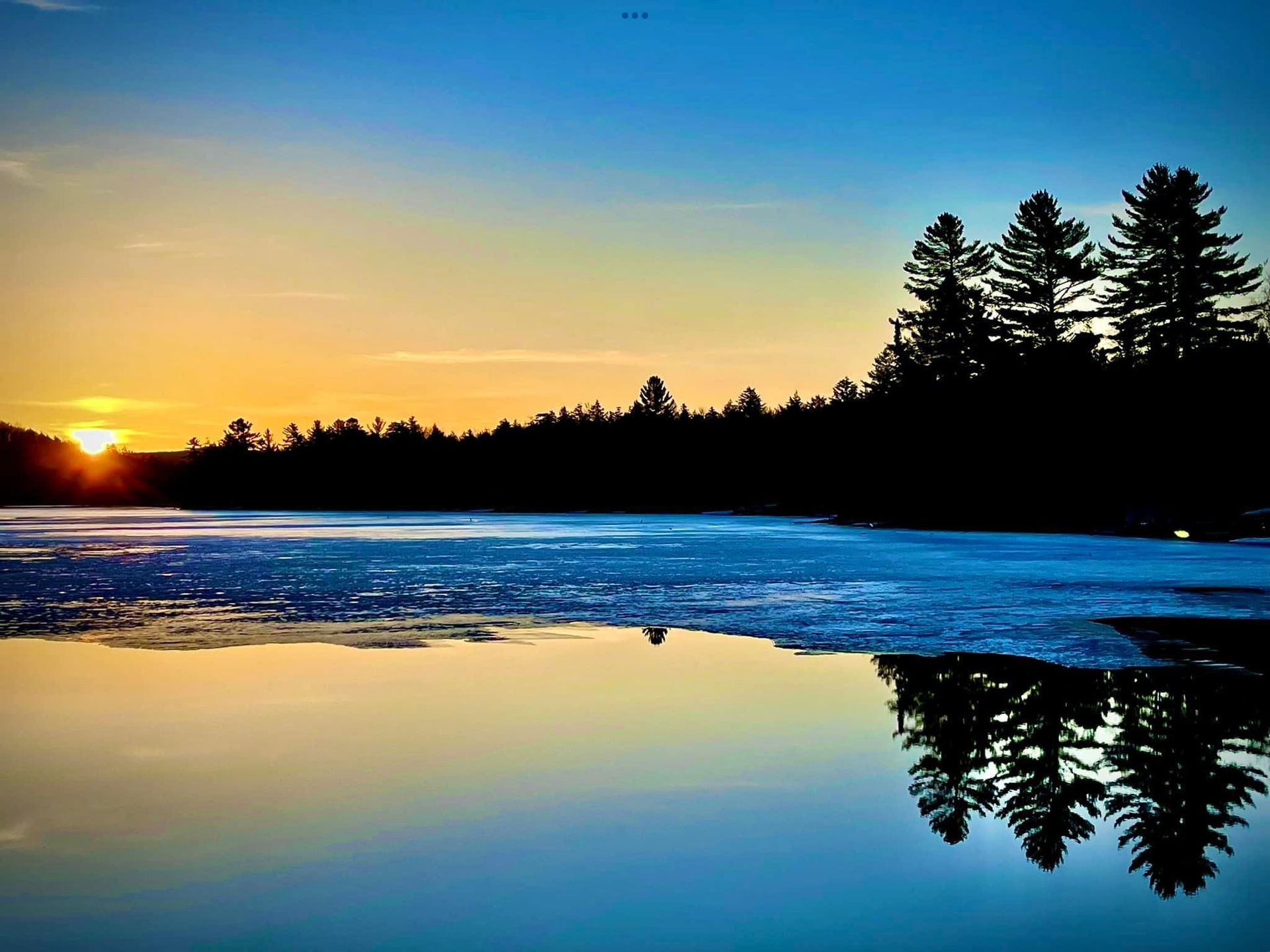 The sun is setting over a lake with trees in the background