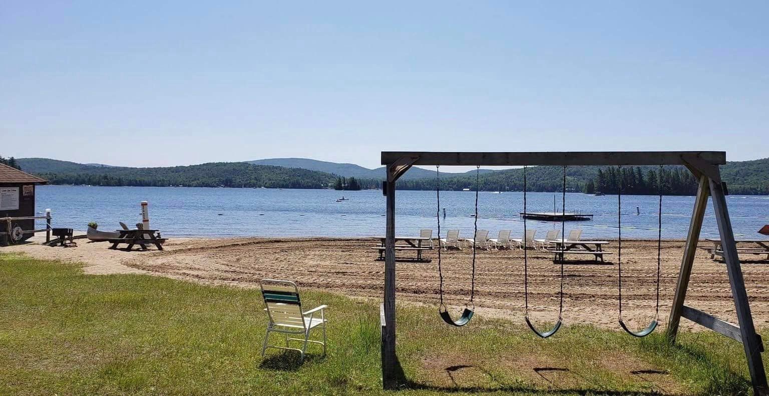 A swing set is sitting on top of a sandy beach next to a lake.