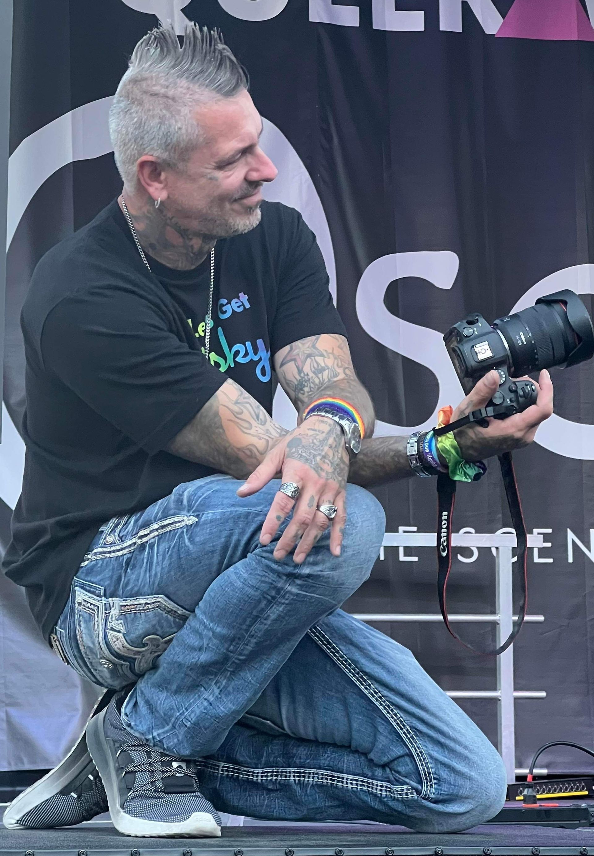 A man is kneeling down holding a camera in front of a sign that says listen