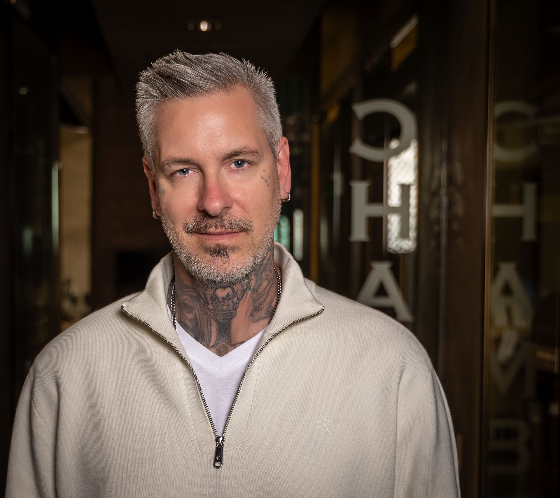 A man with a tattoo on his neck is wearing a white sweater