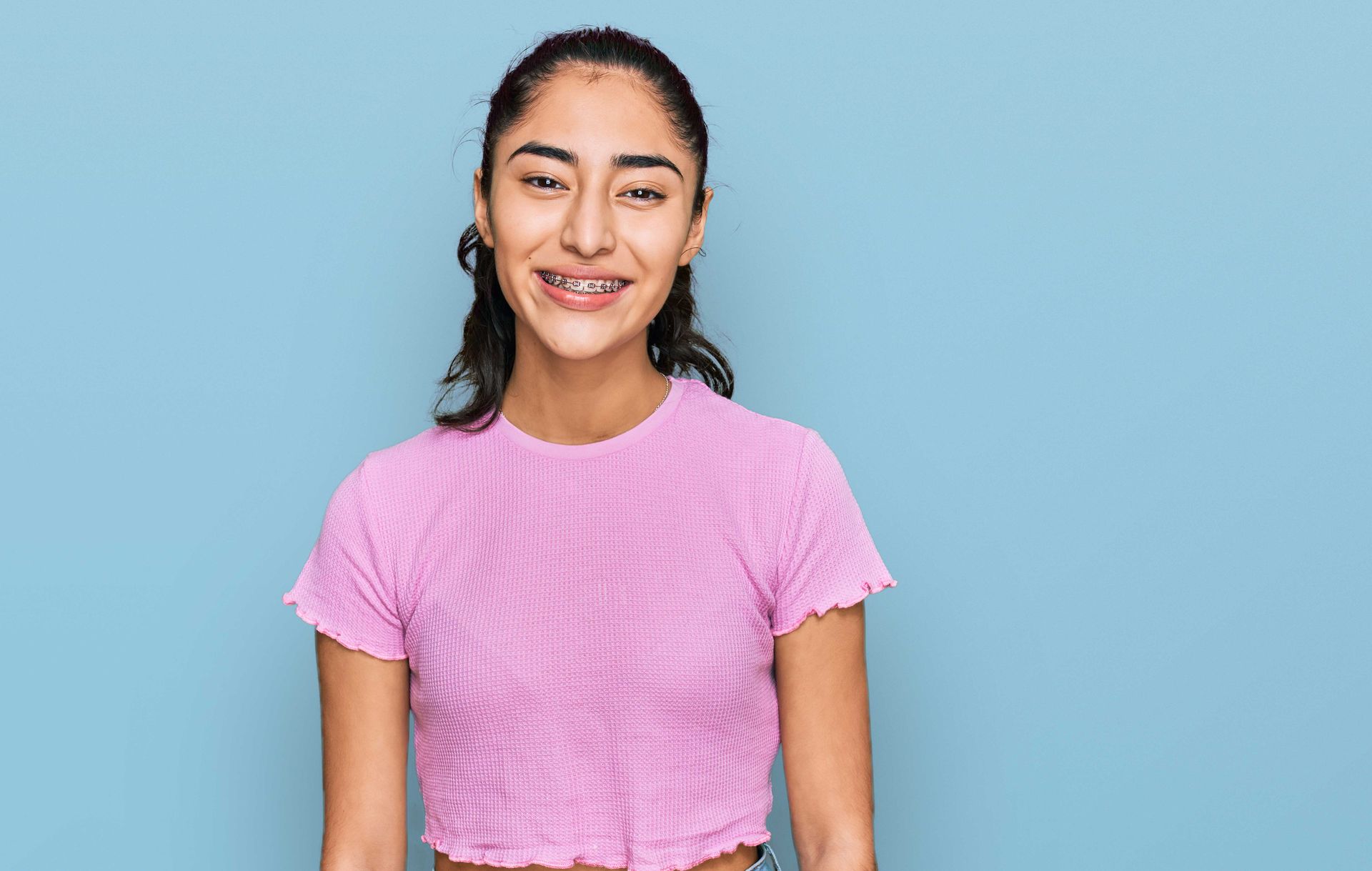 A young woman with braces on her teeth is smiling and looking at the camera.