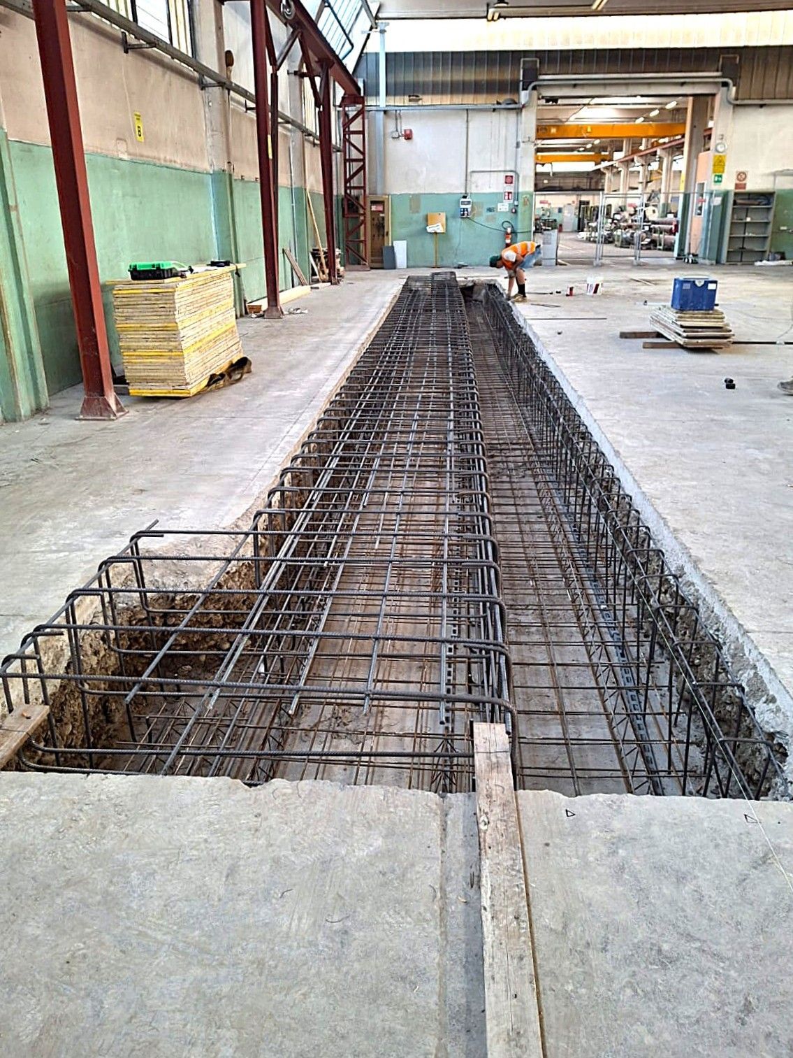 Cantiere: struttura in tondino di ferro in trincea scavata, ambiente industriale.