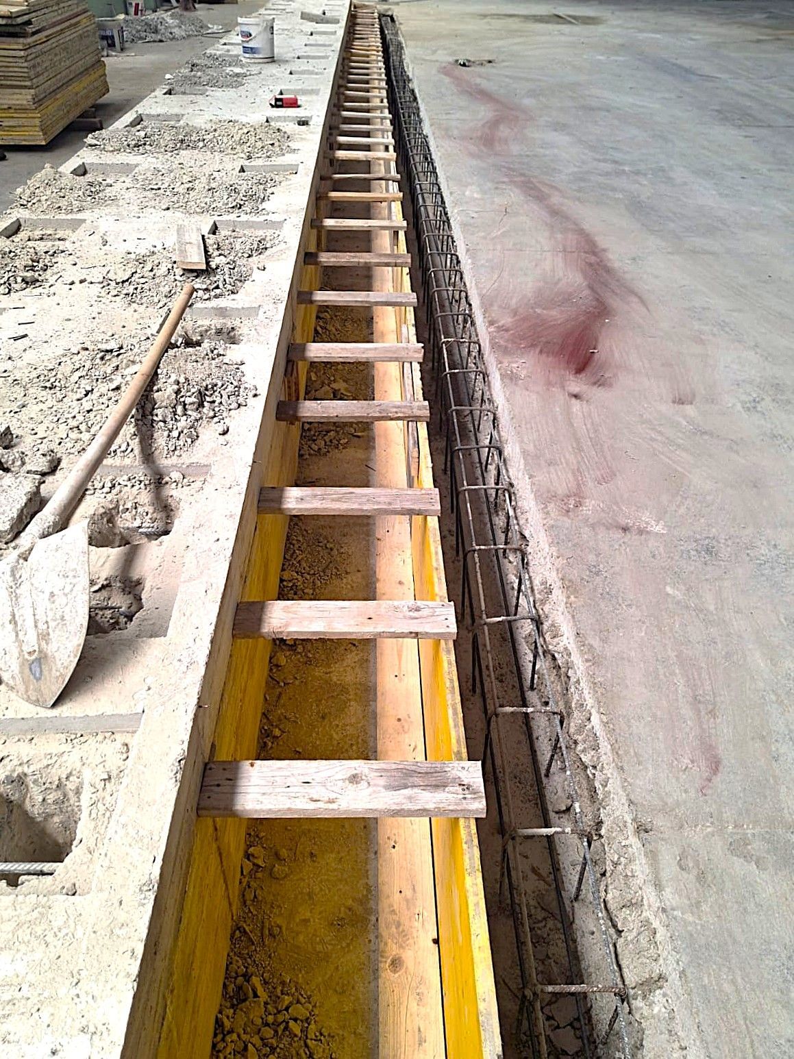 Cantiere con una lunga trincea strutturata con supporti in legno, barre d'acciaio a vista, calcestruzzo.