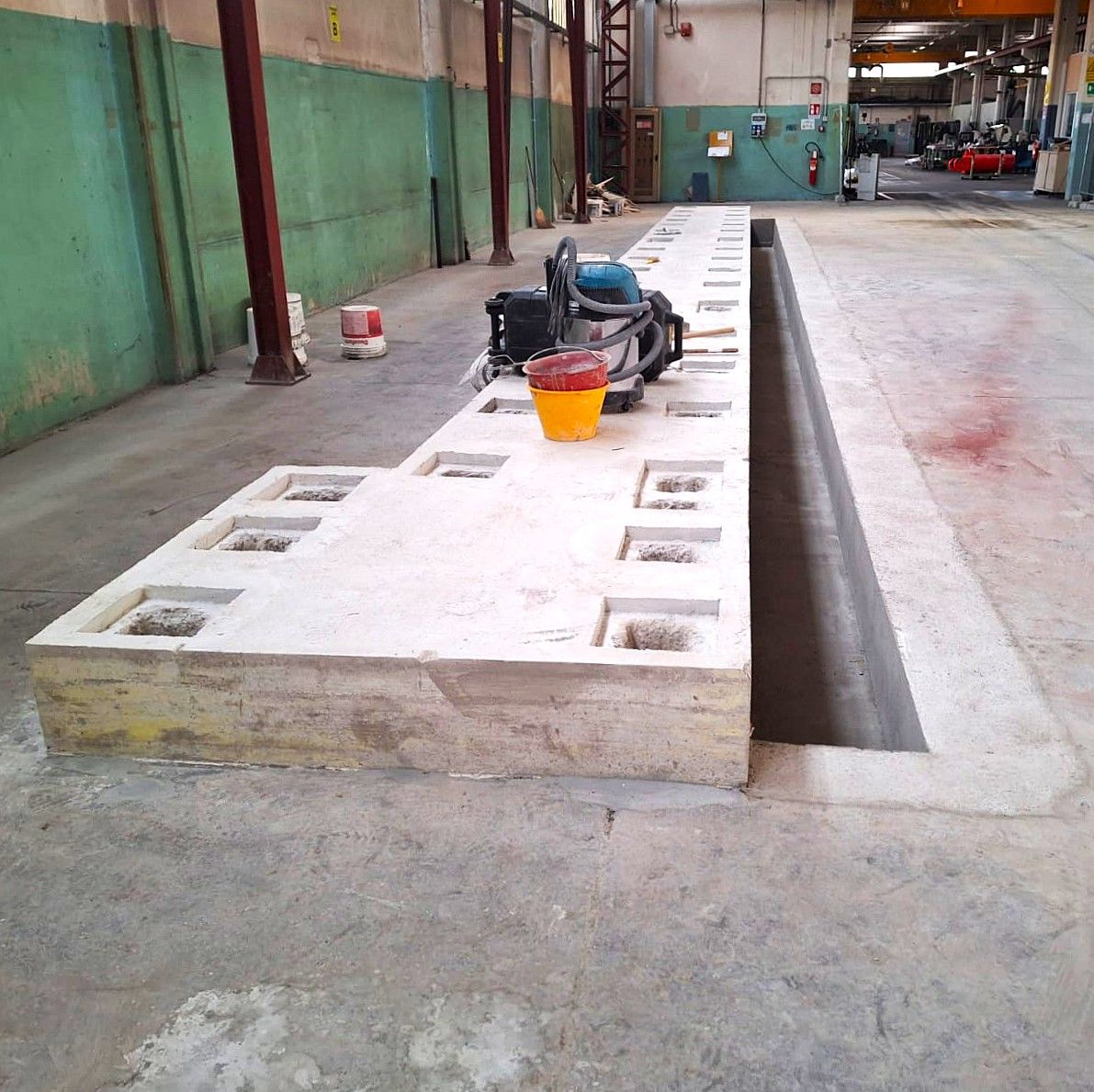 Fossa di ispezione in calcestruzzo in un'officina, con utensili e un secchio in superficie.