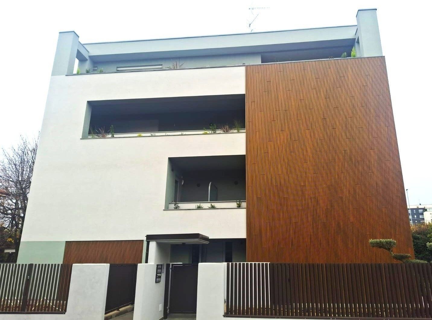 Moderno edificio bianco con pannelli in legno, recinzione e antenna.