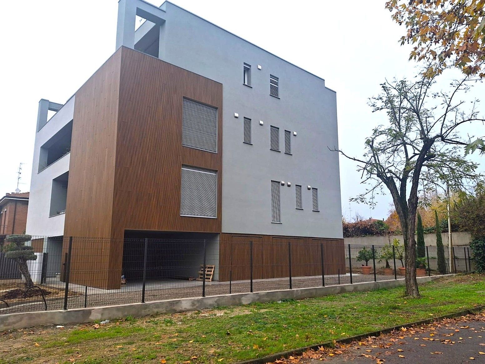 Moderno edificio a più piani con facciata rivestita in legno, perimetro recintato e un po' di verde.