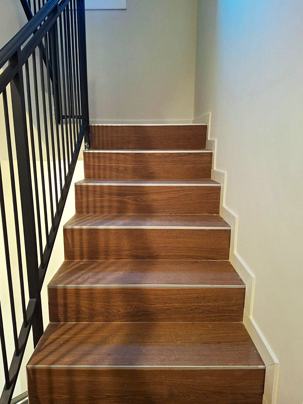 Scala con gradini in legno marrone, ringhiera in metallo nero e pareti bianche.