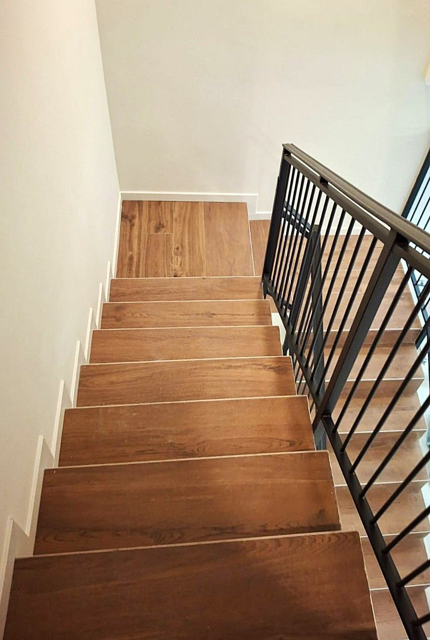 Scala in legno con ringhiera in metallo nero, che scende da una parete bianca.