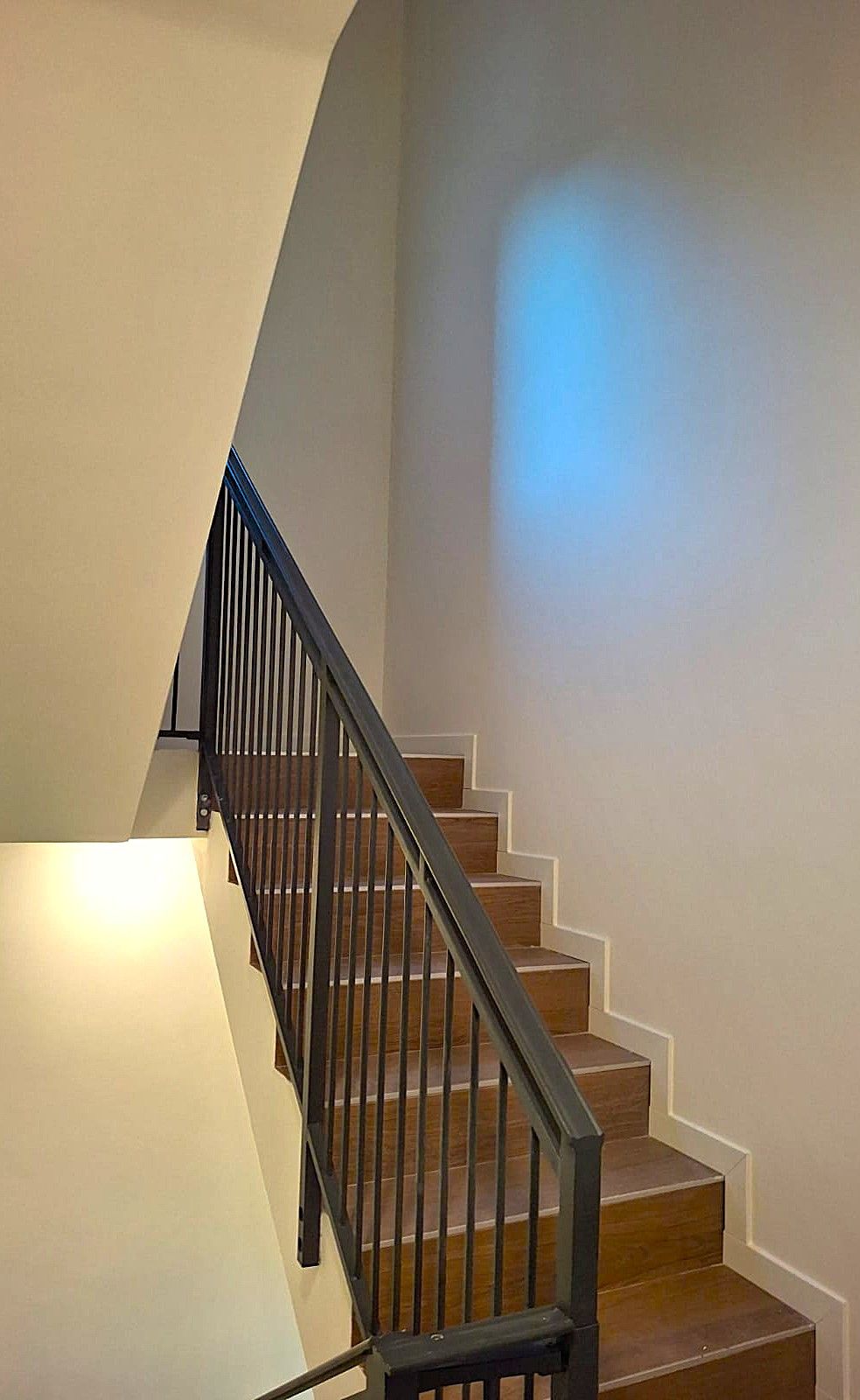 Scala con gradini in legno e ringhiera nera contro pareti chiare.