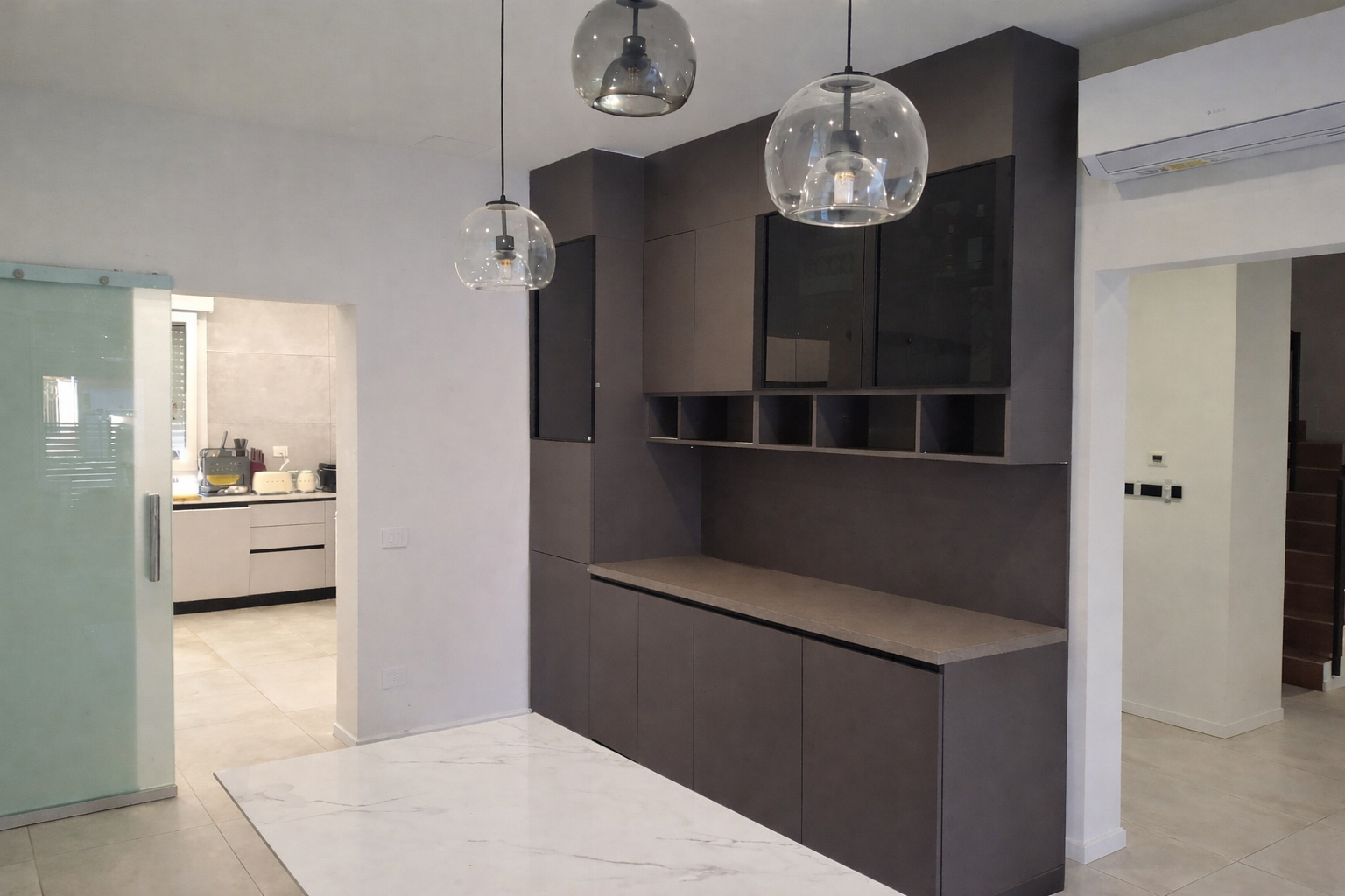 Interni moderni con mobili a muro, lampade a sospensione sferiche e aria condizionata. Una scala conduce al piano superiore.