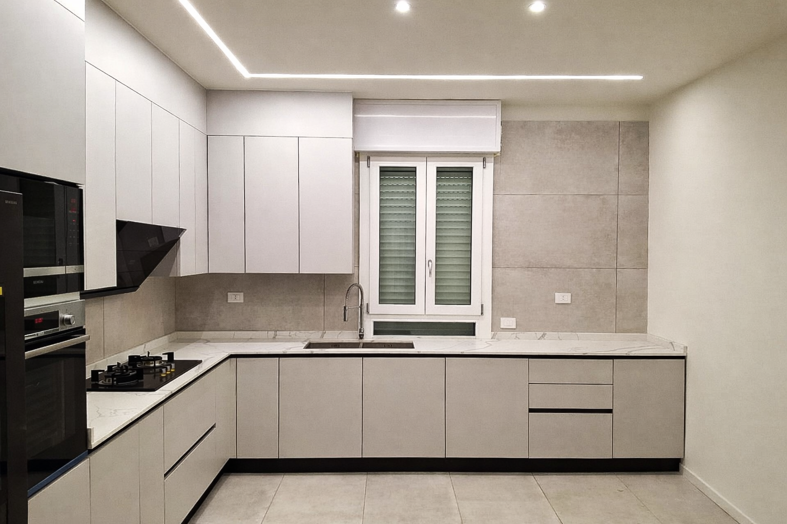 Cucina moderna con mobili grigi, elettrodomestici e una finestra.