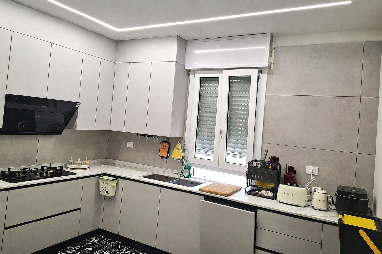 Cucina moderna grigio chiaro con mobili, lavello, finestra, elettrodomestici e piano cottura.