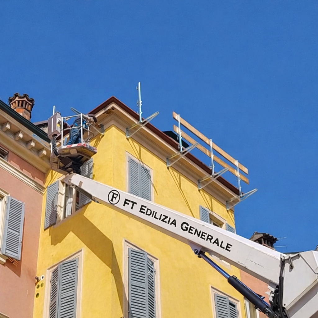 Un edificio giallo ha una piattaforma elevatrice vicino al tetto; sono in corso lavori di costruzione.