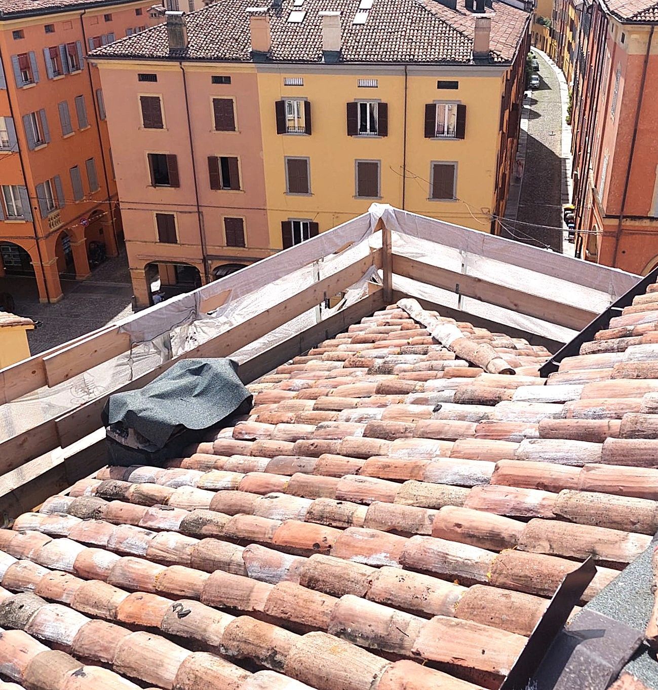 Vista dal tetto di tegole in terracotta, con edifici colorati sullo sfondo. Un telo copre qualcosa sul tetto.