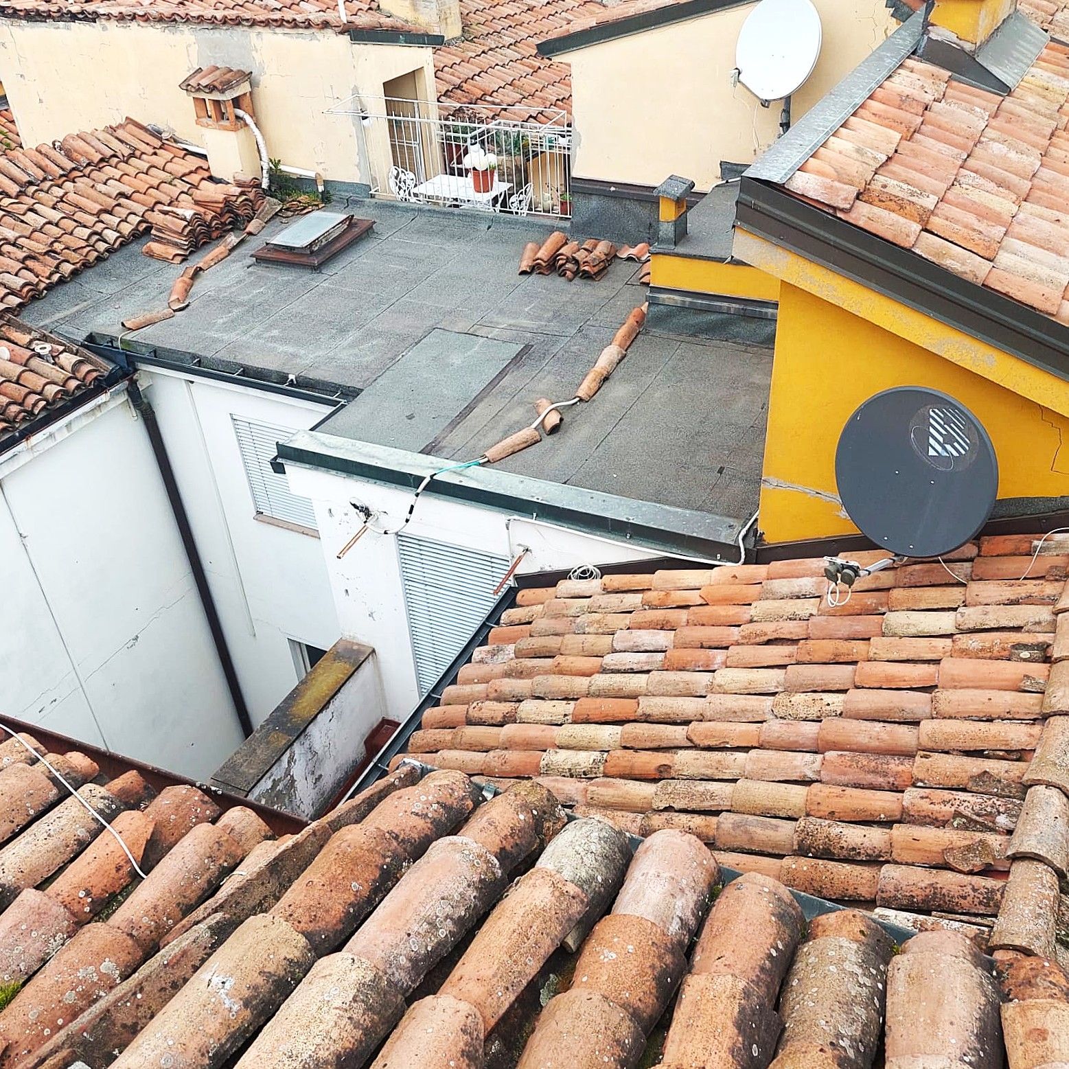 Vista dall'alto di diversi tetti con tegole di argilla, un'antenna parabolica e un pozzo aperto.