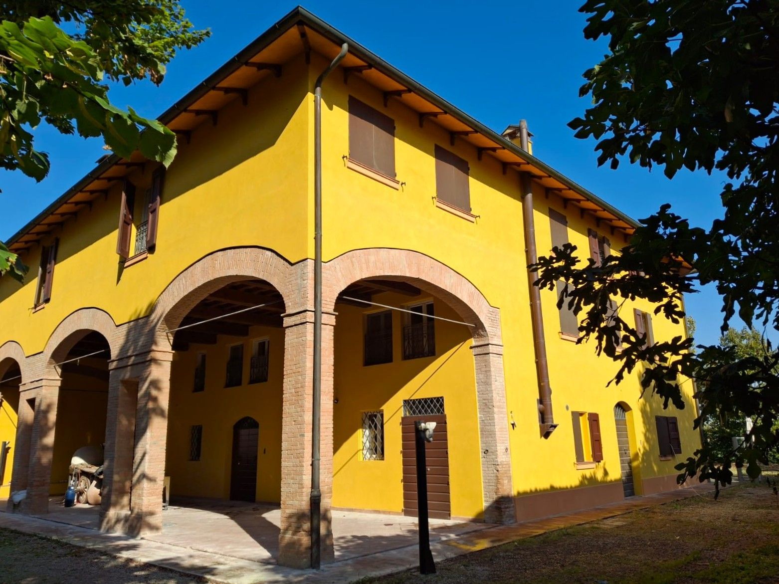 Edificio in stucco giallo con camminamenti in mattoni ad arco sotto un cielo azzurro, circondato da alberi.