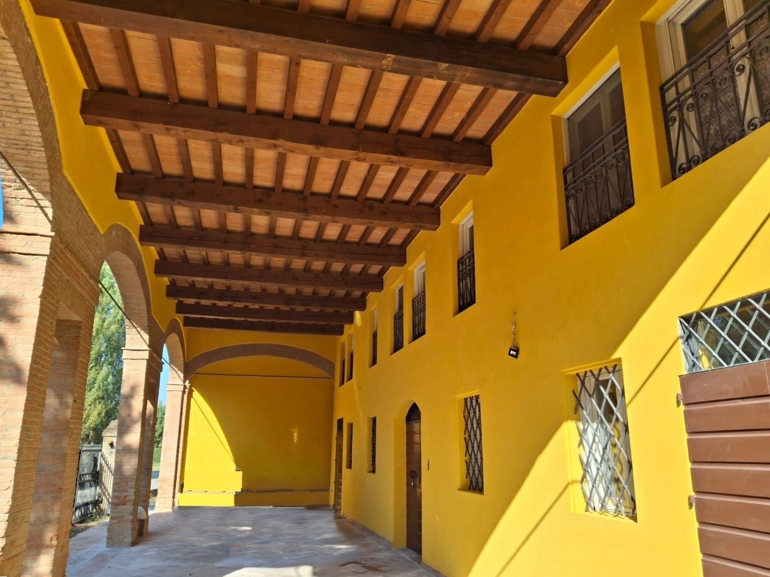 Edificio giallo con passaggio ad arco, travi marroni e finestre con decorazioni in ferro battuto.