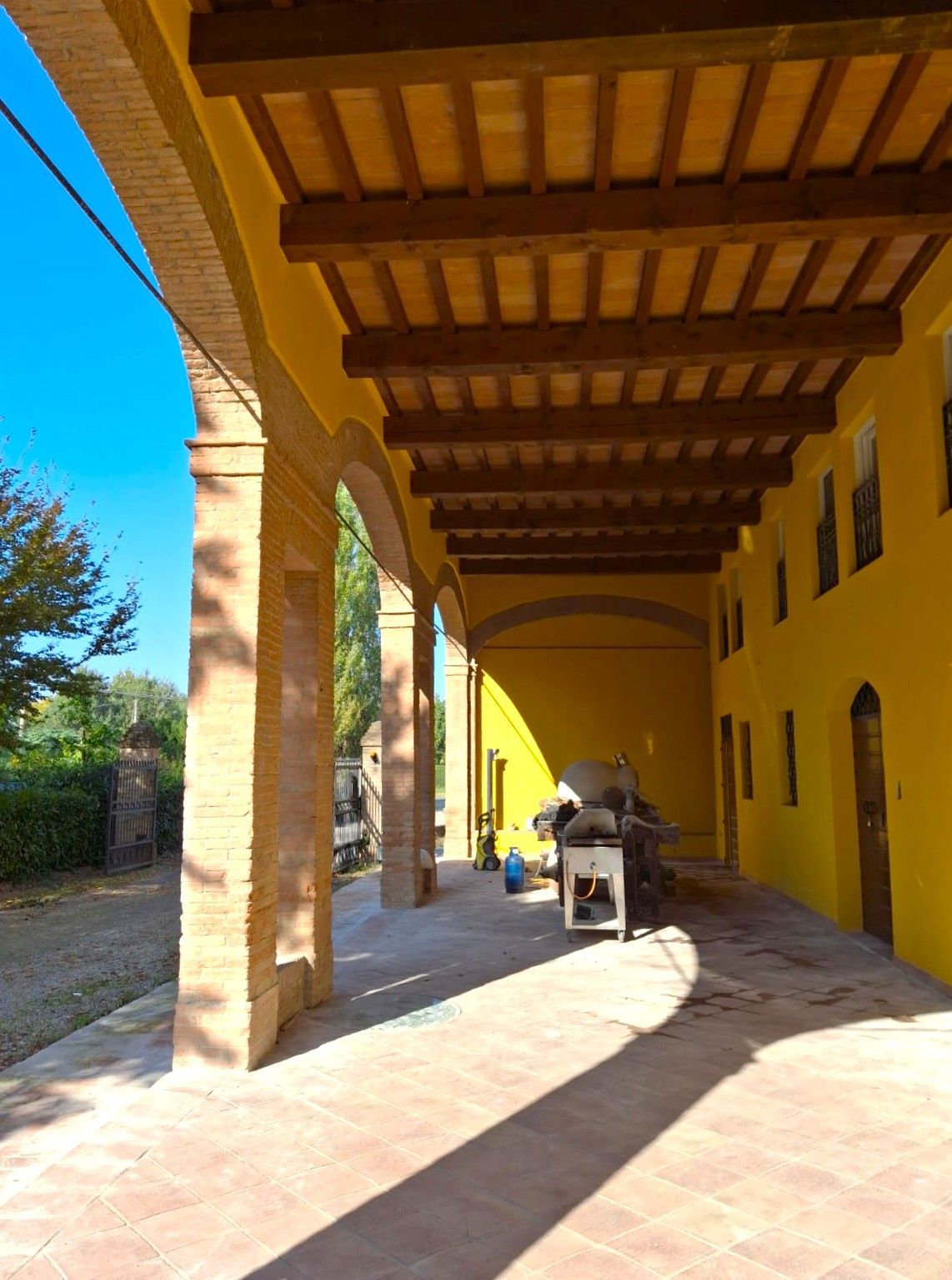 Edificio giallo con passaggio ad arco, colonne in mattoni e soffitto in legno marrone. Giornata di sole.