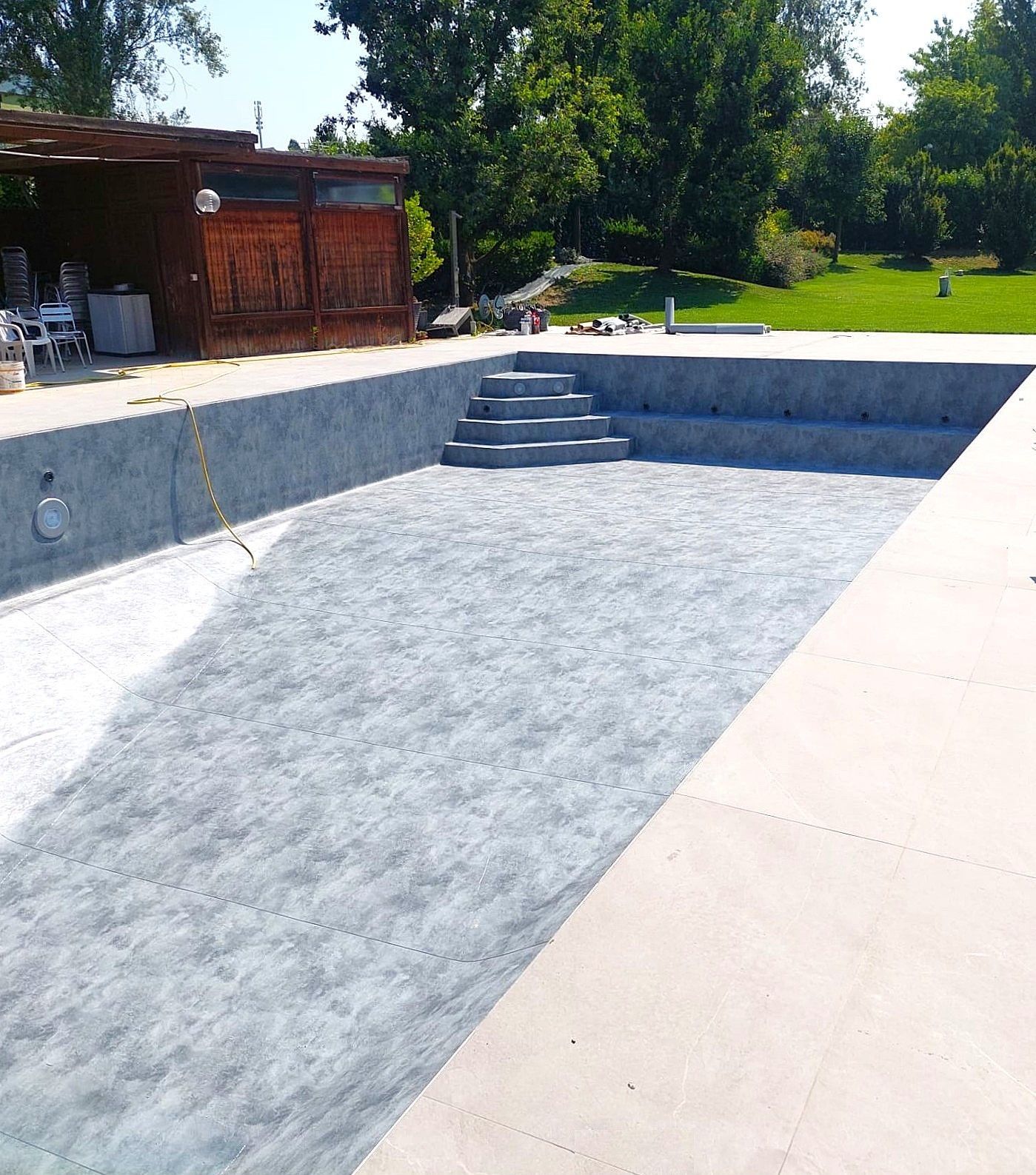 Piscina interrata vuota con interno grigio, gradini in cemento e terrazza circostante in cemento.