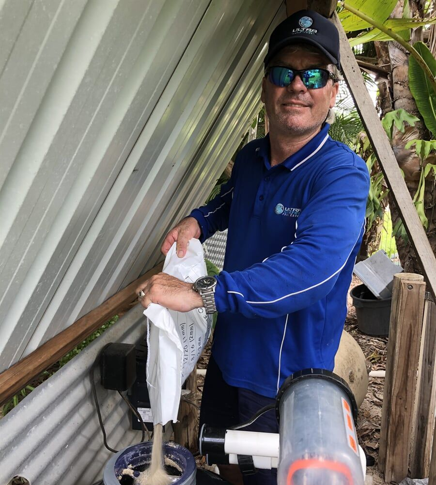Man in Blue Shirt Pouring Sand from A Bag Into a Pool Filter. Outdoors — Ultra Clear Pool Care in Cranbrook, QLD