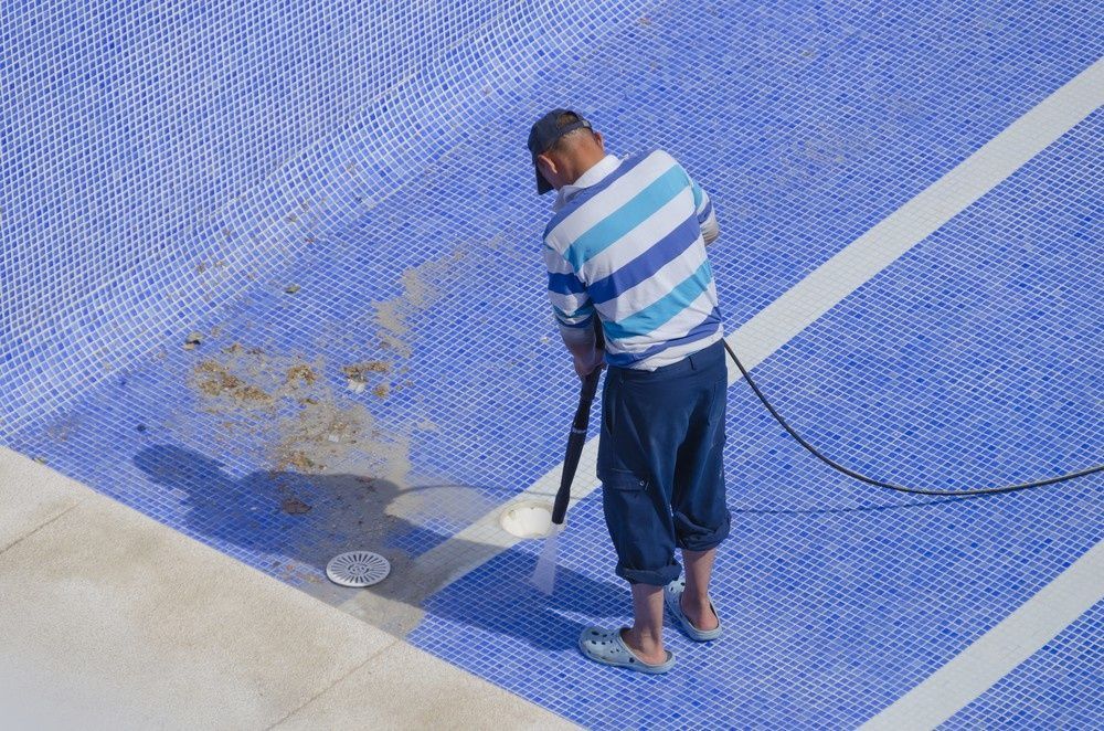Man Cleaning an Empty Blue Swimming Pool with A Vacuum — Ultra Clear Pool Care in Cranbrook, QLD