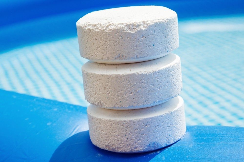Three White Chlorine Tablets Stacked by A Blue Swimming Pool — Ultra Clear Pool Care in Cranbrook, QLD
