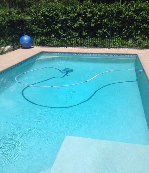 Person Pouring Liquid from A White Jug Into a Blue Swimming Pool — Ultra Clear Pool Care in Cranbrook, QLD
