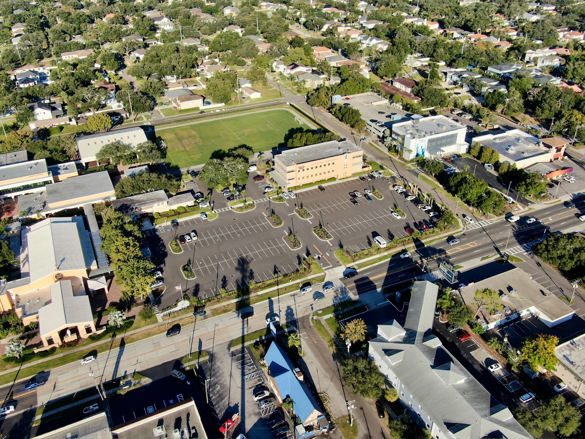 An aerial view shows a suburban neighborhood with buildings, parking lots, green space, and surrounding roads.