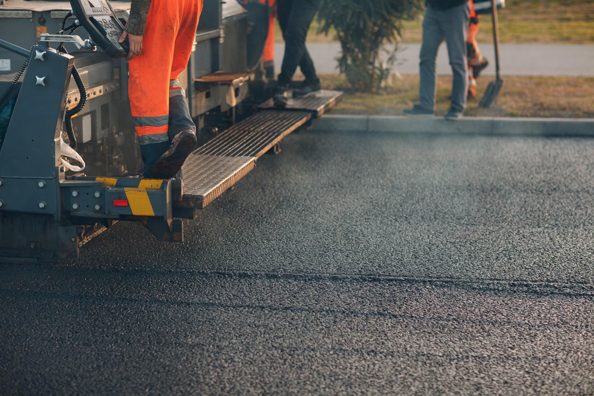 An asphalt paving machine is laying fresh pavement with workers nearby. An asphalt paving machine is laying fresh pavement with workers nearby.