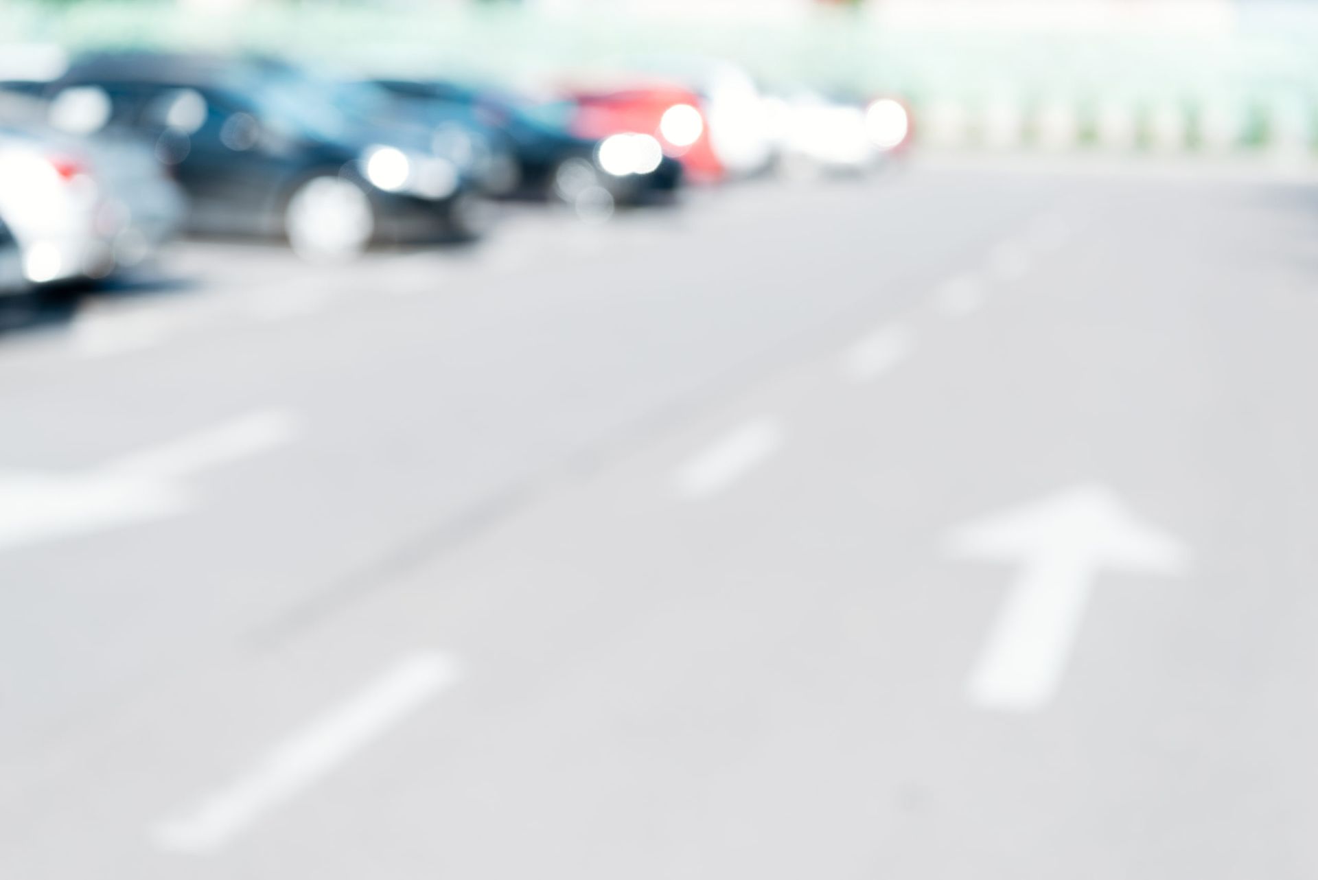 Parking lot with cars parked in a row, white directional arrows on the pavement.