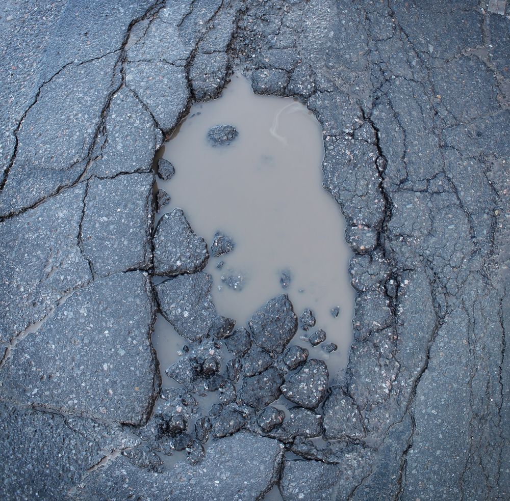 Pothole filled with murky water in cracked asphalt.