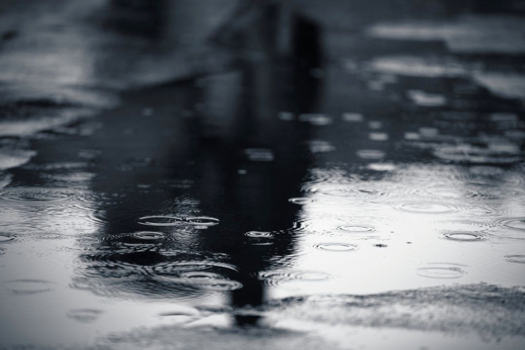 Rainy street: Person's blurred reflection in puddles, drops creating ripples on wet pavement.