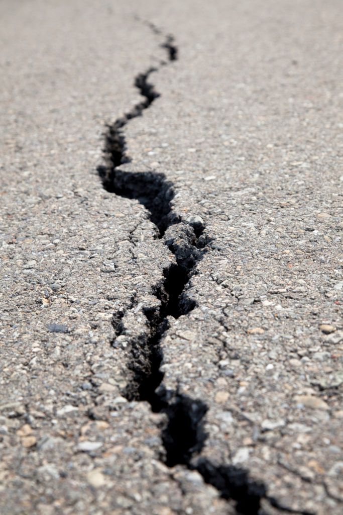 Crack in asphalt road. Dark fissure running through gray surface.