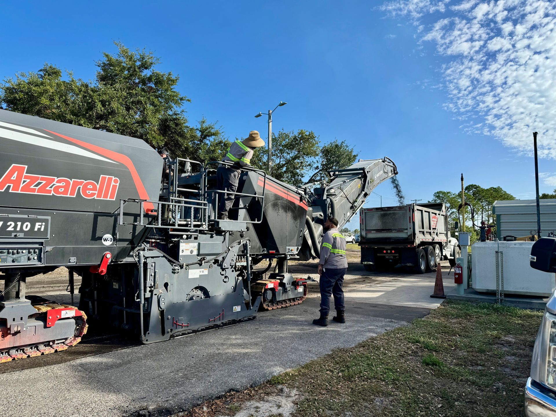 Yellow road milling machine depositing asphalt into an orange dump truck on a highway.