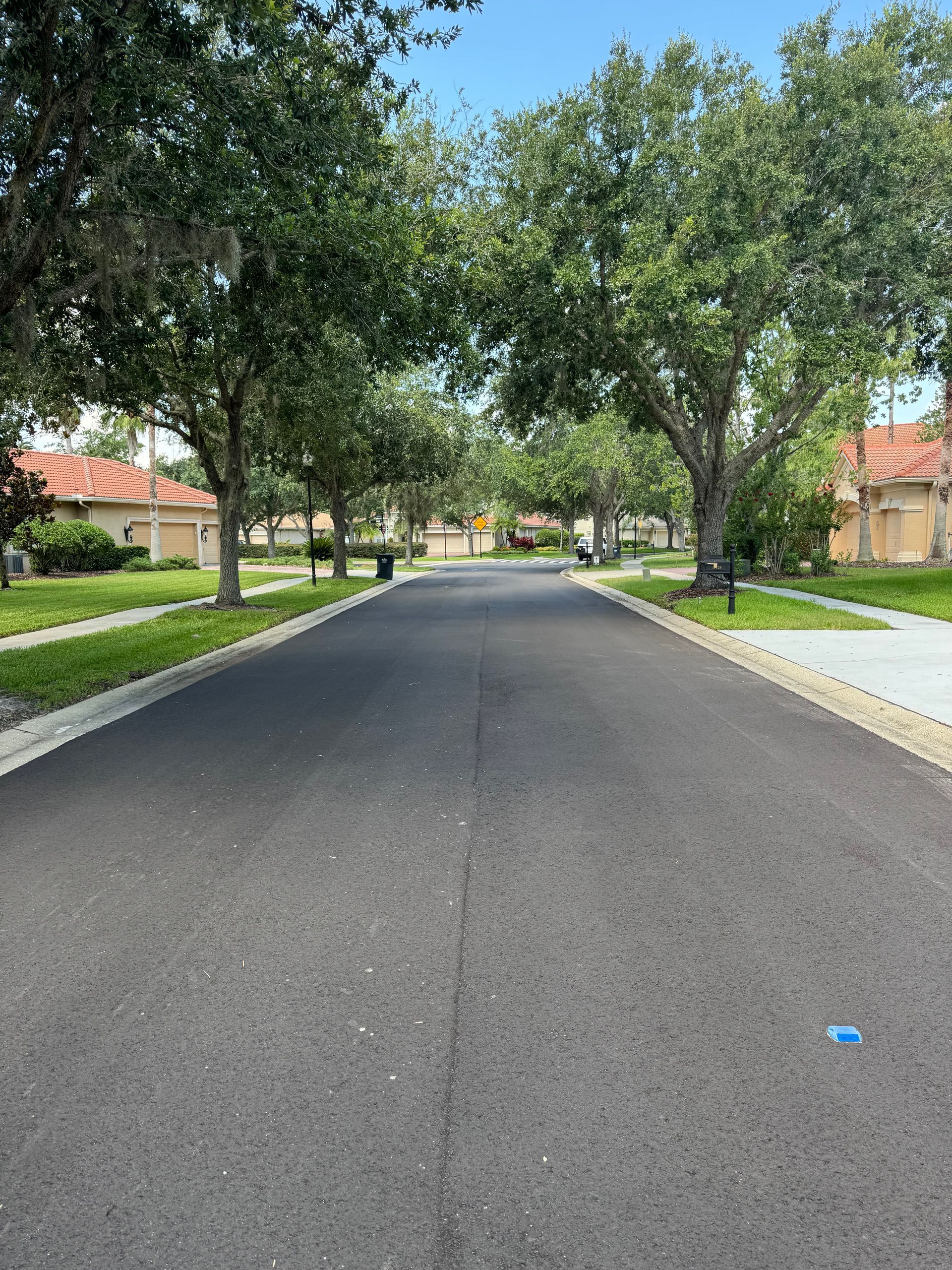 Road worker in safety vest, leveling asphalt with a rake near paving equipment.