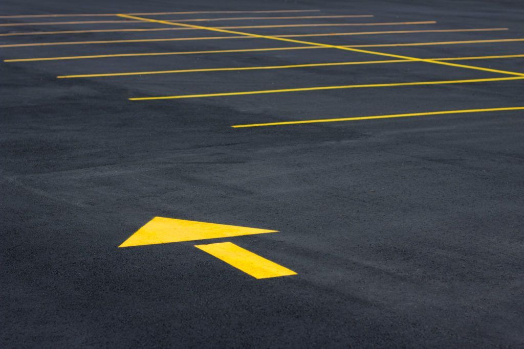 Yellow arrow pointing left on asphalt parking lot with yellow parking lines.
