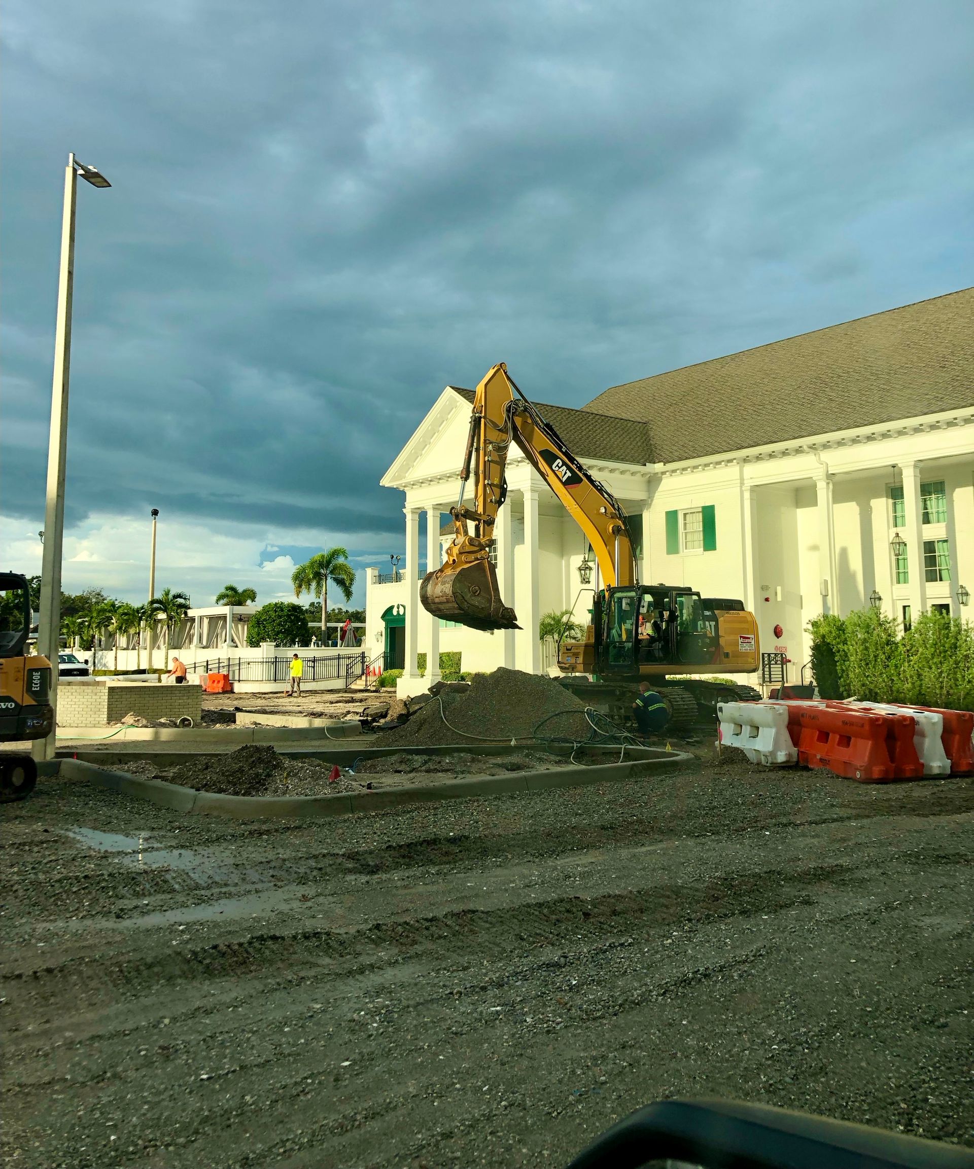 An excavator and loader working at a gravel pit under a blue sky, near a dump truck and pile of gravel.