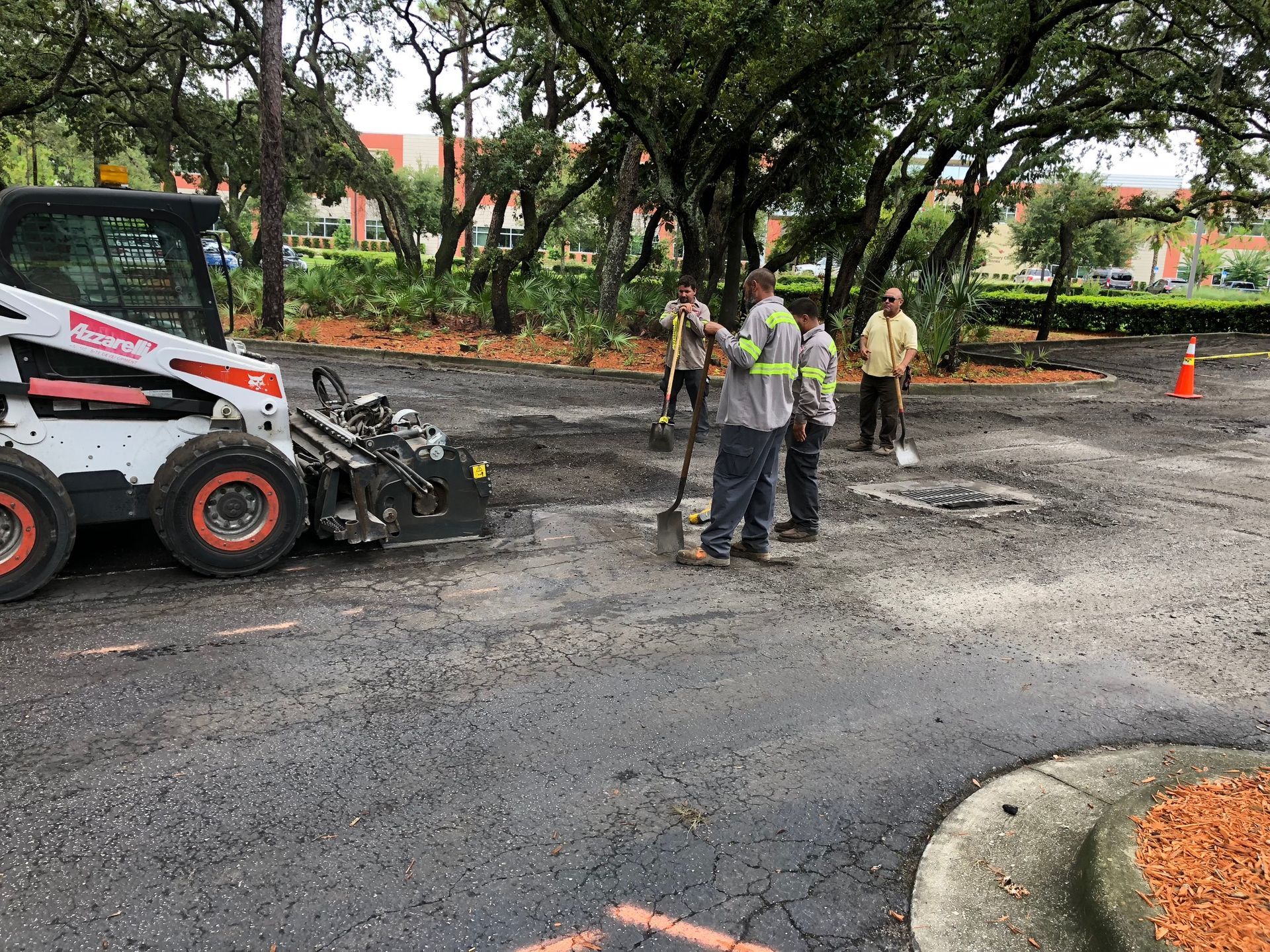 Workers by a Bobcat preparing asphalt in a parking lot.