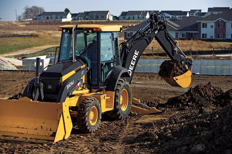 Yellow and black John Deere backhoe digging dirt on a construction site.