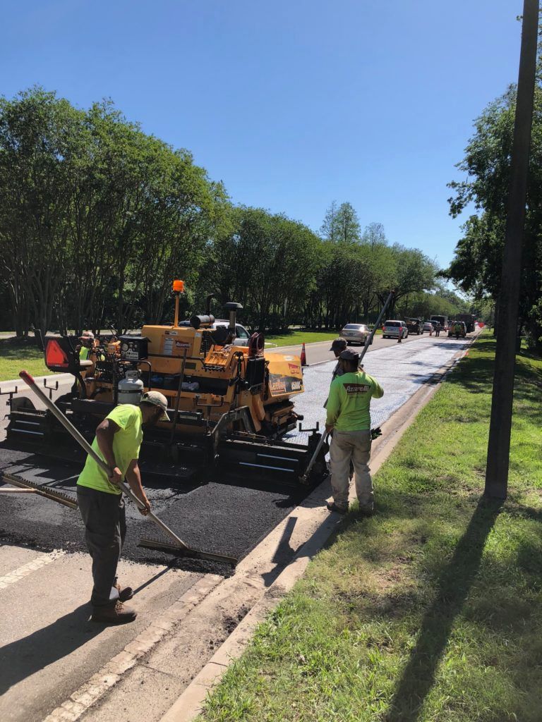Road crew paving a street on a sunny day. Workers in safety vests use tools and a paving machine.